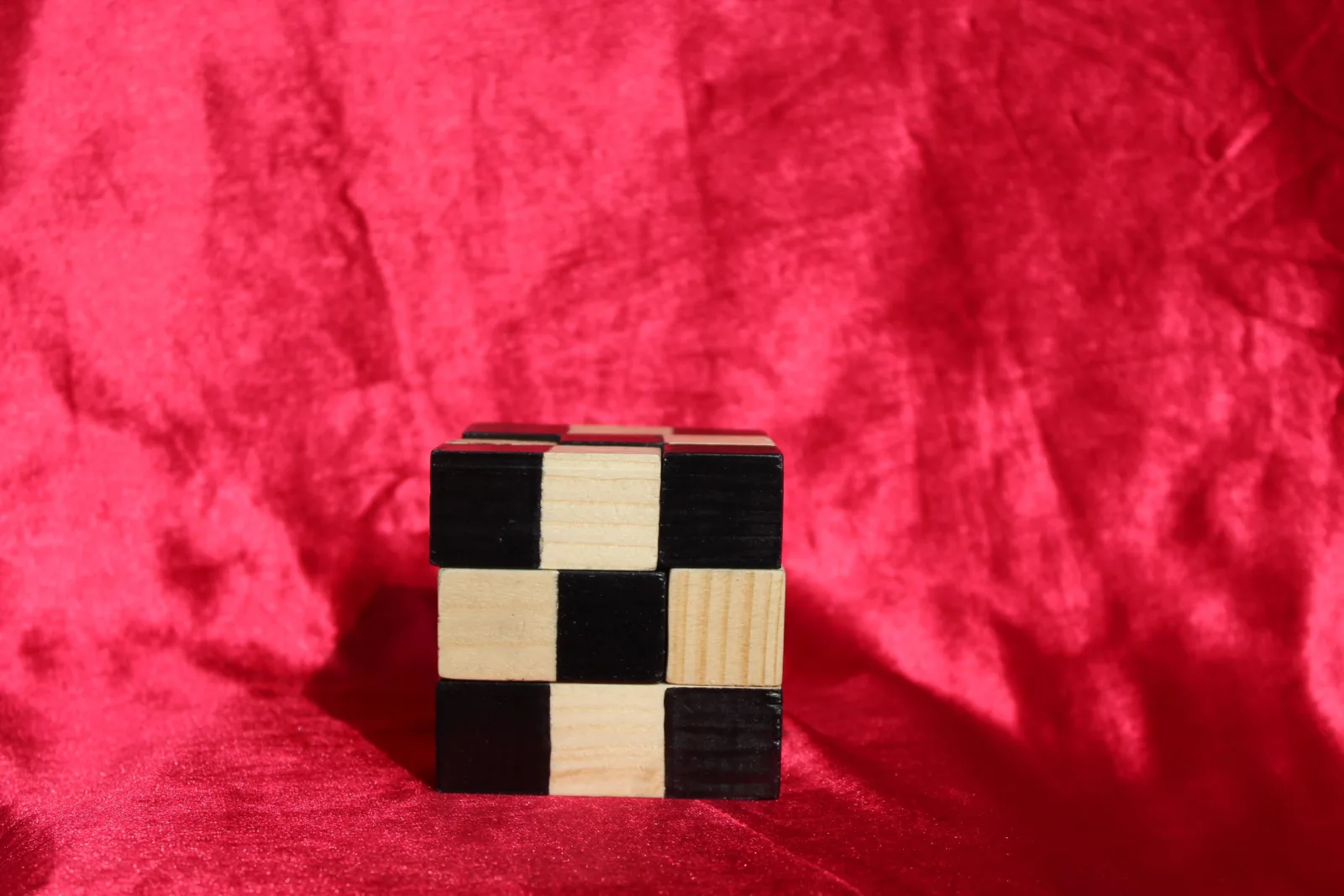 Petit cube en bois à damier noir et naturel, posé sur un tissu rouge