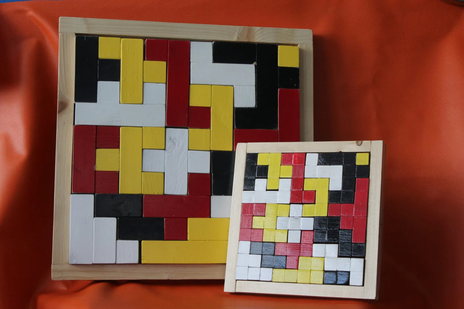 Deux casse-têtes en bois de tailles différentes, pièces laquées rouge, jaune, noir et blanc, posés sur un tissu orange
