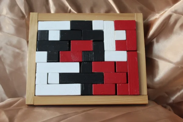 Casse-tête Matrice Tricolore : pièces rouges, noires et blanches dans un cadre rectangulaire en bois clair