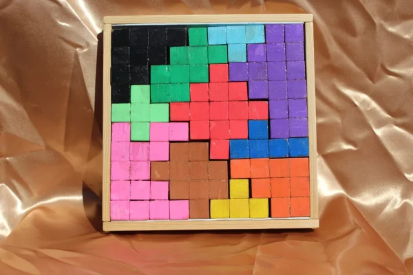 Casse-tête Mosaïka : pièces roses, violettes, vertes et orange dans un cadre carré en bois clair